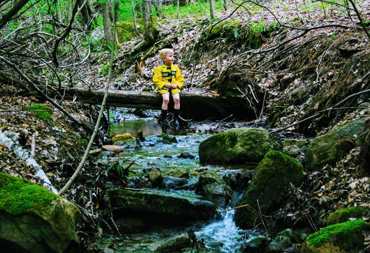 Horizon Homeschool Child sitting on log over stream, Horizon Homeschool